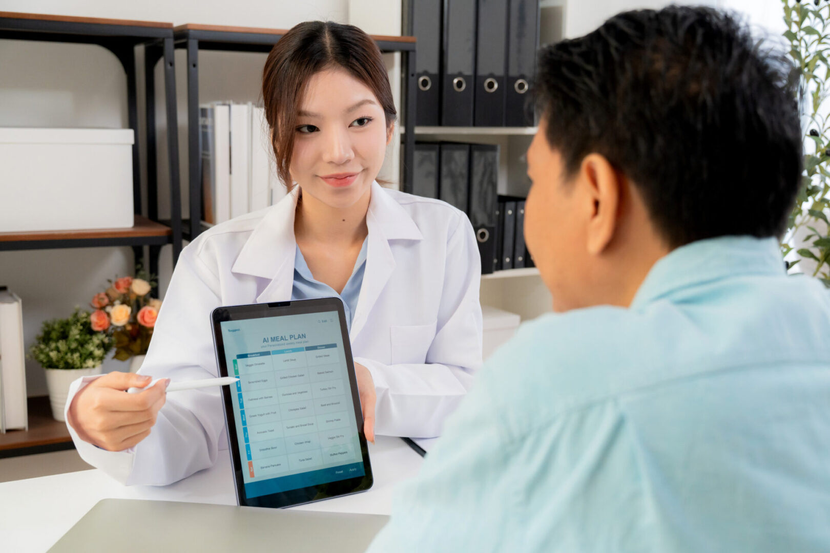 Asian nutritionist using tablet to explaining personalized meal plan with AI to patient during healthcare consultation, healthy lifestyle, woman dietitian showing nutrition plan with AI on tablet.